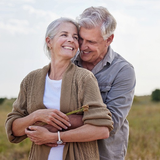 Couple smiling while hugging in field outside