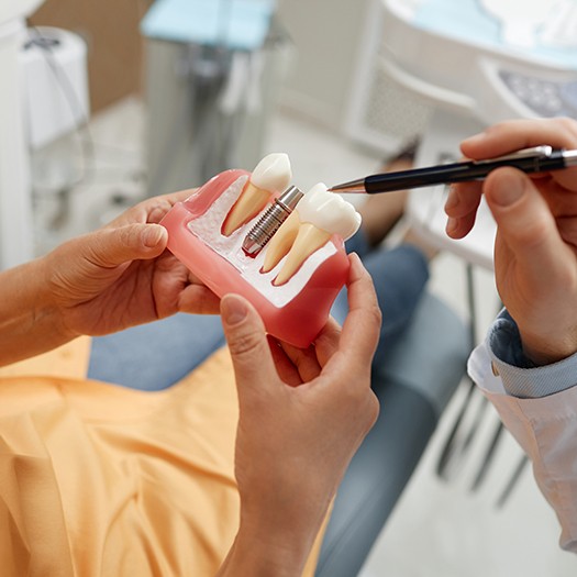 a dentist and patient examining a dental implant model
