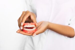Person in white jacket holding set of dentures.
